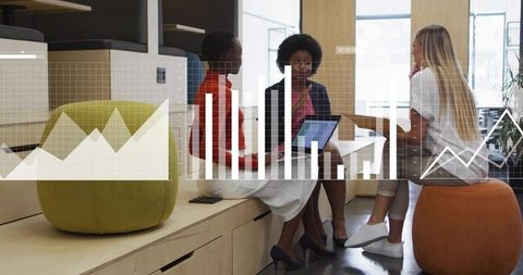 Female colleagues collaborating over laptop with graph overlays in modern office lounge