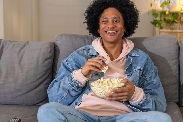 African american man relaxing on couch with popcorn enjoying cozy movie night