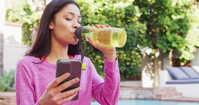 Biracial woman using smartphone and drinking water in garden. Beauty, health and female spa home concept.