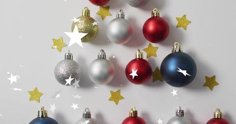 Holiday baubles forming triangular tree flatlay with gold star confetti on gray surface