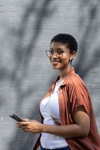 Young african woman using smartphone and smiling against gray brick wall