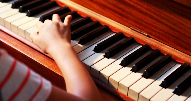 This image captures a close-up view of a child's hand playing on a piano keyboard, emphasizing artistry and practice. Useful for educational materials, music lesson promotions, and articles on child development through music.