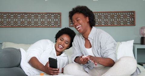 Happy Friends Laughing with Smartphone in Cozy Living Room