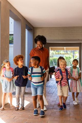 African american teacher leading diverse elementary students walking in school corridor