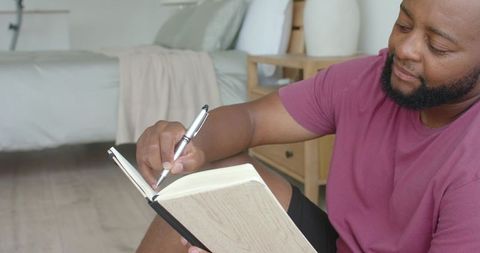 Man writing in journal on bedroom floor with natural light minimalist home journaling mindful