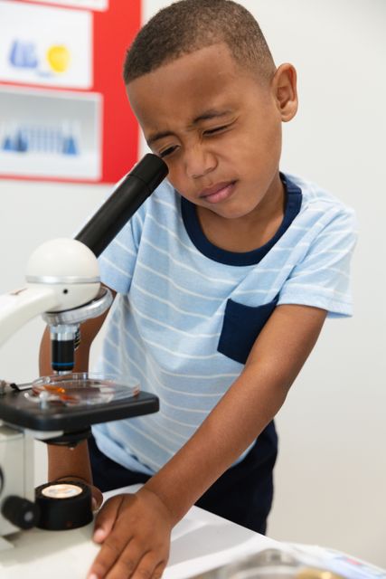 Young African American boy using a microscope in a chemistry class, focusing intently on his experiment. Ideal for educational materials, STEM promotion, school brochures, and science-related content.