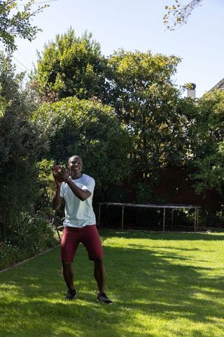 Athletic man catching football outdoors in green backyard
