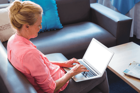 Senior woman using transparent laptop at home on sofa