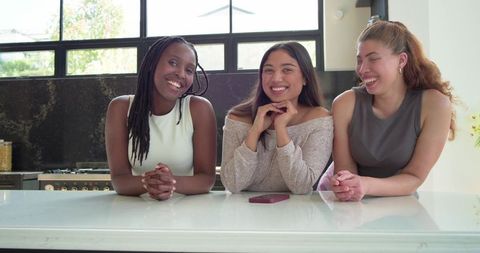 Three friends leaning on kitchen island smiling and laughing with smartphone