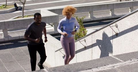 Diverse couple running stairs in urban plaza wearing sportswear and fitness watches
