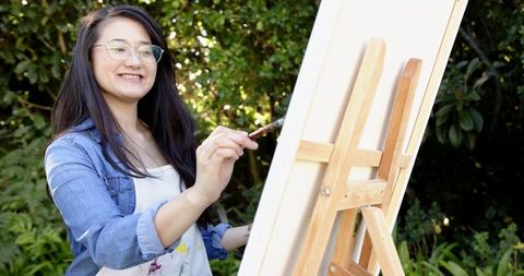 Smiling Artist Paints on Easel in Lush Garden Setting