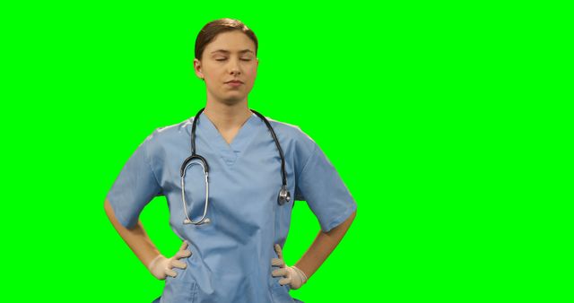 Female healthcare professional standing confidently with eyes closed, wearing blue scrubs and stethoscope against green screen background. Perfect for healthcare promotion, medical presentations, or advertisements requiring a customizable green screen.