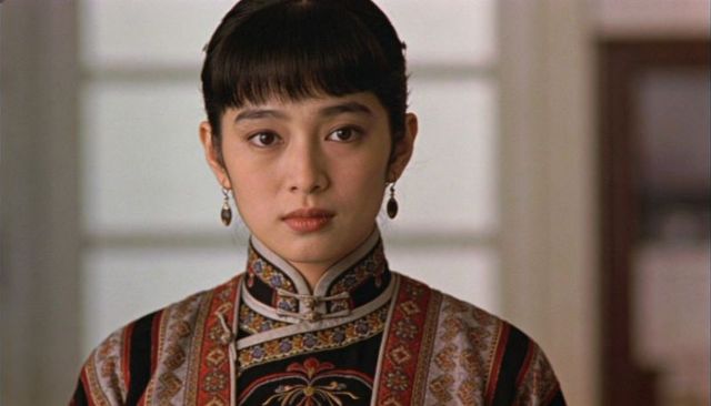 Elegant asian woman wearing embroidered high collar brocade robe standing by frosted window
