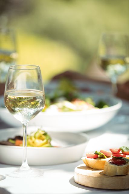 This image showcases a close-up view of a wine glass filled with white wine and various appetizers on a dining table in a restaurant. Ideal for use in advertisements for restaurants, culinary blogs, and promotional materials for fine dining experiences.