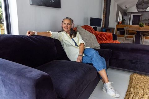 Mature woman relaxing on velvet sectional listening to music with headphones in open living room