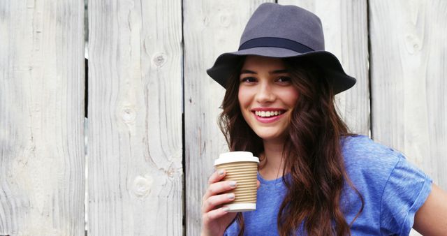 A young Caucasian woman smiles while holding a coffee cup, with copy space on the wooden background - Download Free Stock Photos Pikwizard.com