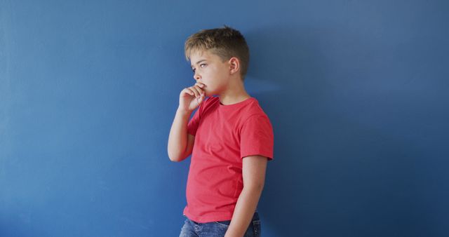 Thoughtful Young Boy Standing Against Blue Wall in Red Shirt - Download Free Stock Images Pikwizard.com