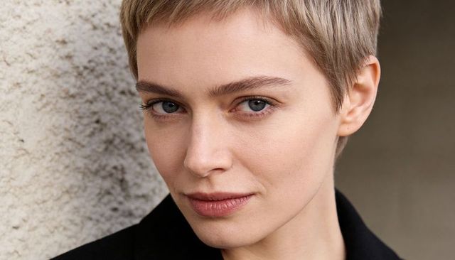 Short blonde pixie hair woman meeting gaze against stucco wall close-up portrait