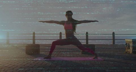 Practicing warrior ii at sunrise on ocean boardwalk for outdoor yoga and fitness