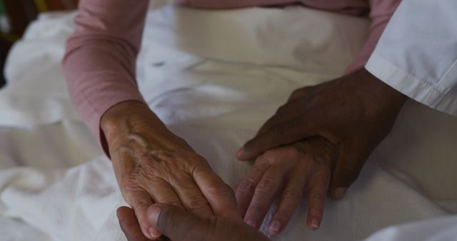An elderly person's hands being held by a healthcare professional showing support and care. Ideal for use in healthcare, elderly care, support services, and medical themes highlighting compassion and assistance in treatment.
