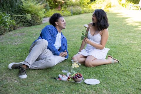 Sunlit garden picnic: african american man and asian woman sharing romantic rose moment