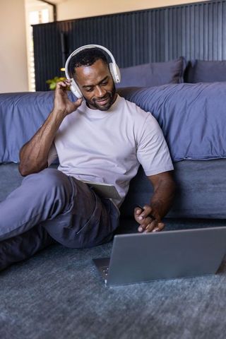 Mature african man studying remotely with headphones, using laptop and tablet