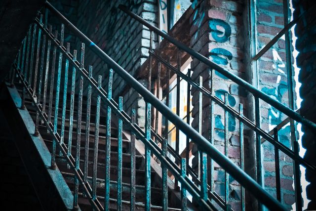 Shows rusty metal staircase with graffiti-covered walls in abandoned building. Ideal for illustrating urban decay, industrial themes, or exploring forgotten places. Suitable for use in projects on urban exploration, architectural studies, or gritty backdrops.