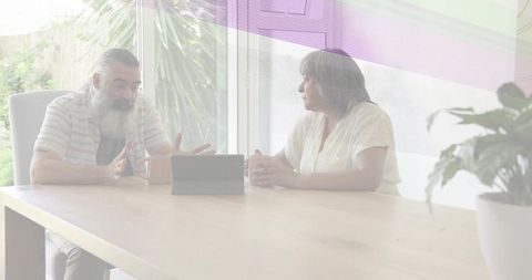 Gesturing bearded man and listening senior woman conversing at sunlit wooden table