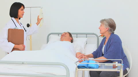 nurse holding clipboard stands by a hospital bed where a middle-aged patient lies receiving care. beside him, a supportive visitor sits providing comfort. this scene involves healthcare provision, patient-nurse interaction, and hospital environment, useful for illustrating medical care settings, compassionate healthcare, or family support in hospitals.