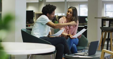 Colleagues collaborating over documents in modern open-plan office lounge with laptop