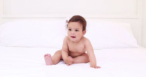 Adorable Baby Sitting on White Bed Looking Curious