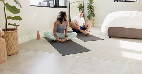 Diverse Couple Practicing Seated Stretches in Bright Bedroom