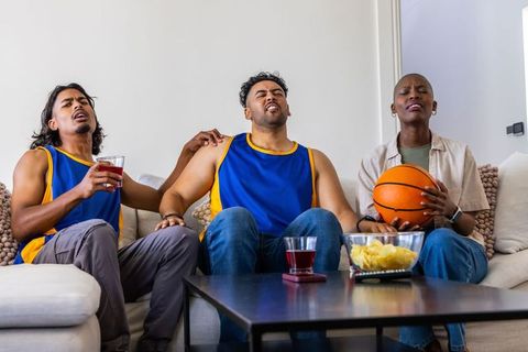Multicultural friends reacting to tense basketball game while watching at home on couch