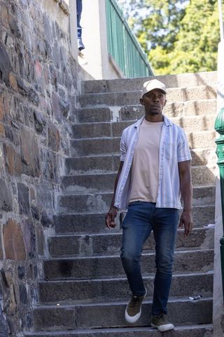 African american man walking down urban stone steps wearing cap and casual summer outfit