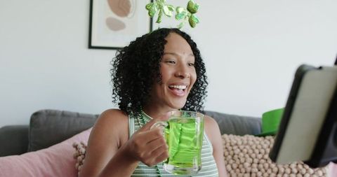 Joyful african american woman celebrating st patrick's day at home holding green beverage