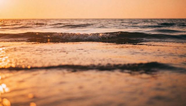 Golden sunset shoreline with gentle breaking waves and warm reflections