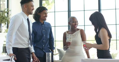 Diverse young professionals socializing in chic lounge with cocktails and bright grid windows