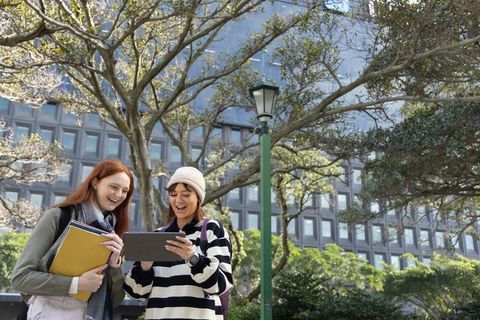 College friends sharing tablet outdoors on campus near lamppost and trees