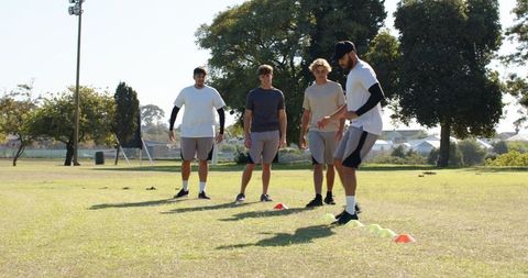 Male athletes practicing cone agility drill on grass field during outdoor team training