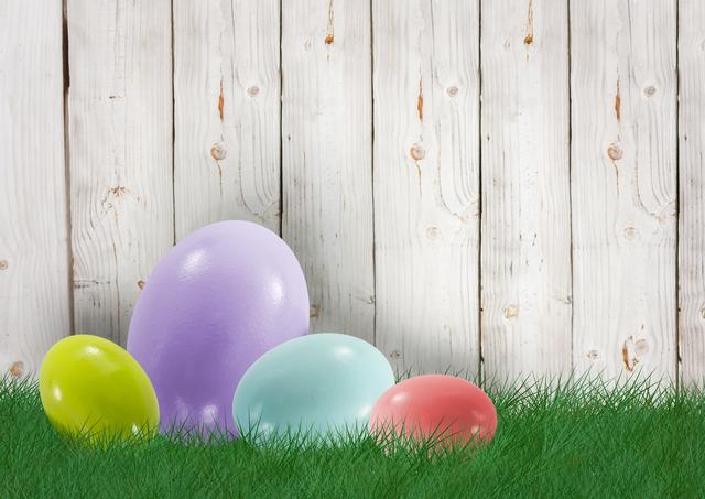 Easter eggs of different colors are placed on green grass in front of a wooden fence. This bright and cheerful image is perfect for use in festive holiday promotions, Easter greeting cards, spring event announcements or decorations, and social media posts celebrating Easter.