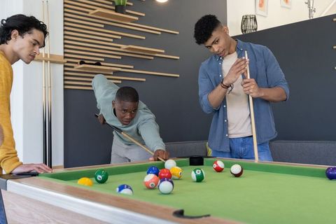 Multicultural male friends playing pool in modern game room casual billiards night