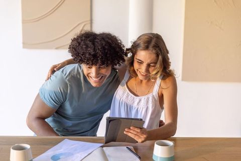 Young couple sharing tablet smiling and planning finances together at cozy home workspace