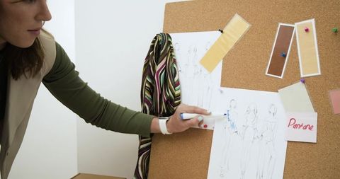 Fashion designer marking moodboard sketches with blue marker on corkboard