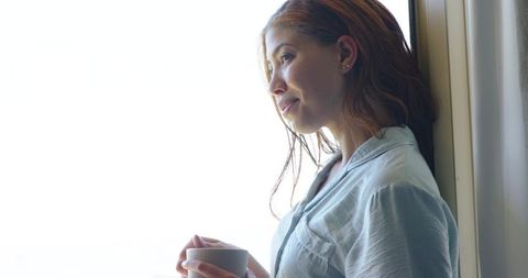 Contemplative woman leaning by window holding mug, morning calm, natural backlit portrait