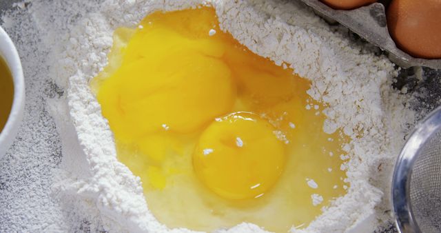 This stock photo features raw egg yolks placed in a pile of flour, capturing the initial stages of baking preparation. Ideal for use in cooking tutorials, recipe blogs, or culinary advertisements highlighting the start of a baking project.