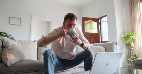 Mature Man Enjoys Coffee While Working from Cozy Home Sofa