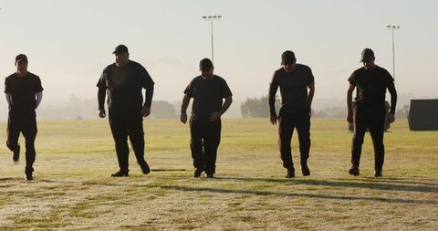 Backlit team marching across morning training field wearing dark uniforms and caps