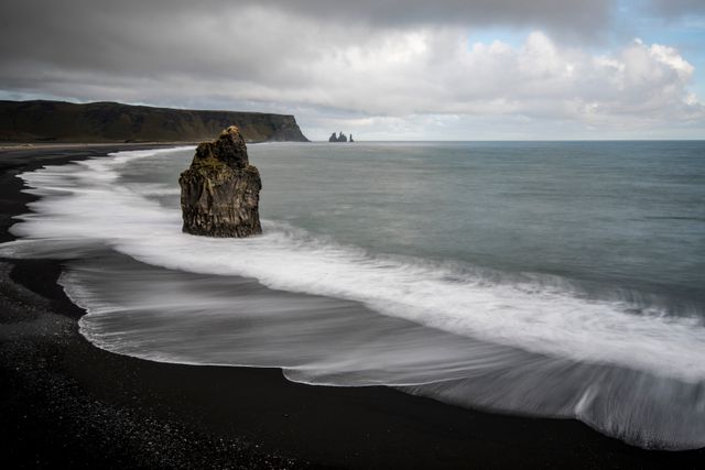 Majestic view of Iceland's black sand beach with towering rock formations against the dramatic sky and gentle waves. Ideal for travel guides, nature documentaries, and magazines focusing on stunning landscapes and natural wonders. Perfect for promoting Iceland as a tourist destination or for use in calendars featuring beautiful coastal sceneries.