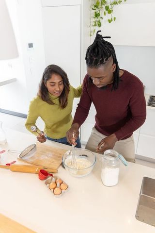Diverse couple whisking batter on kitchen island, home baking teamwork in modern kitchen