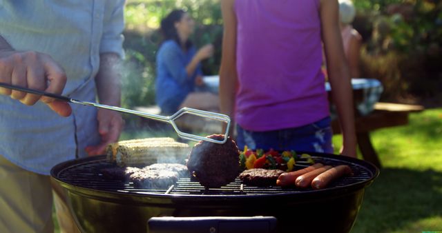 A person is grilling food on a barbecue in an outdoor setting, with diverse individuals in the background enjoying a sunny day. Capturing the essence of a summer gathering, the image evokes the joy of casual outdoor dining and socializing.